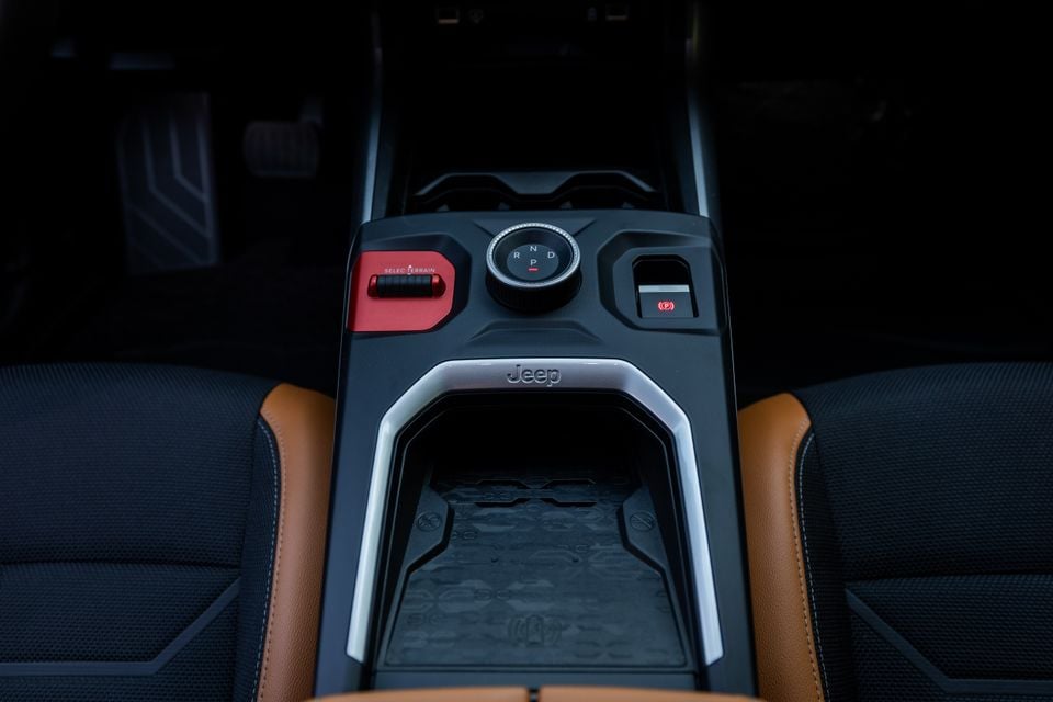 Jeep Compass centre console showing the rotary gear selector, red Selec-Terrain dial, electronic parking brake button, and open storage bin with tan leather seat bolsters on either side