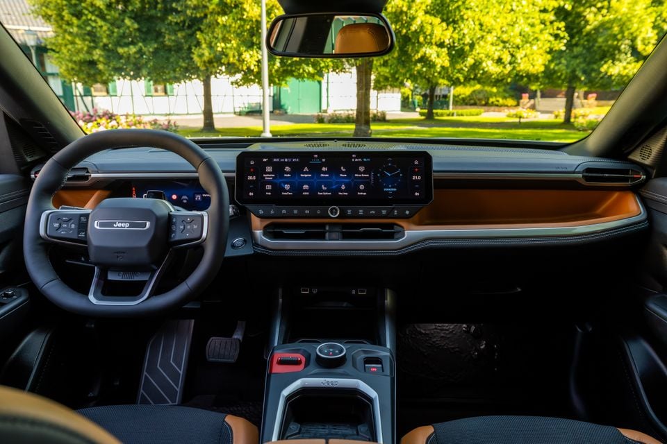 Interior of a Jeep Compass showing the steering wheel, wide touchscreen infotainment display, and tan leather dashboard trim