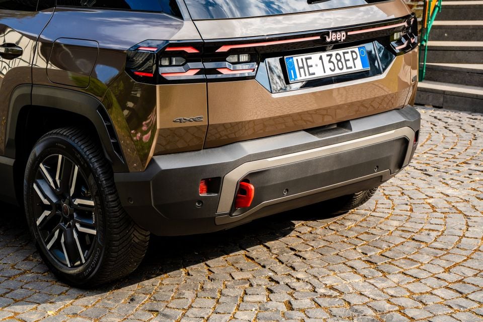 Rear of a bronze 2027 Jeep Compass 4xe SUV on a cobblestone street, showing taillights, bumper detail and licence plate