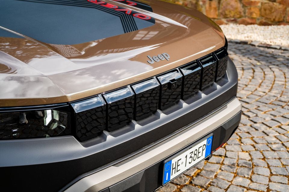 Close-up of the front grille and hood of a 2027 Jeep Compass, showing the seven-slot grille design and Jeep badge, parked on cobblestones.