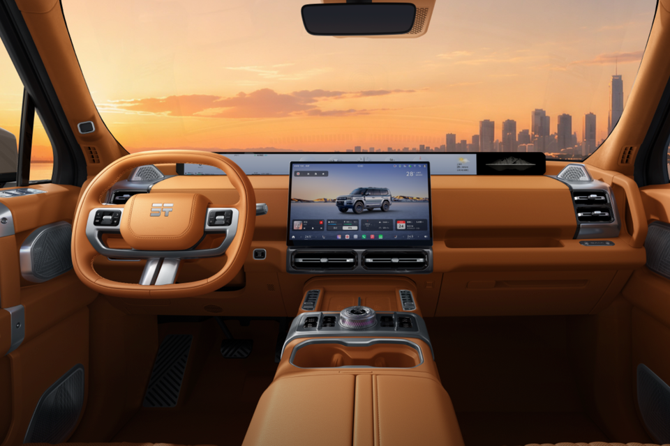 Tan leather dashboard of the 2027 Jetour G700 with a squared-off steering wheel, large central touchscreen and a city sunset beyond the windscreen