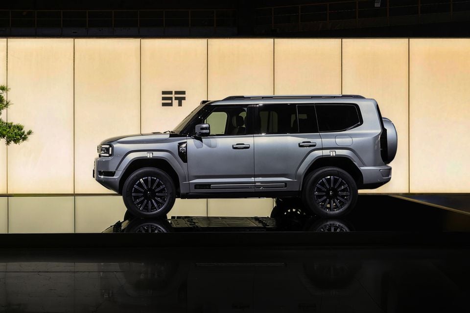 A silver 2027 Jetour G700 SUV seen side-on, with a rear-mounted spare wheel, displayed against a backlit wall