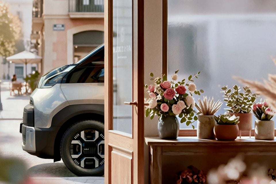 A Kia EV SUV parked on a city street, seen from the front side, framed by an open doorway with flowers and potted plants in the foreground