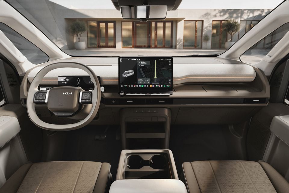 Interior of a Kia PV7 showing the dashboard, large central touchscreen with navigation displayed, Kia-branded steering wheel, and light-coloured front seats