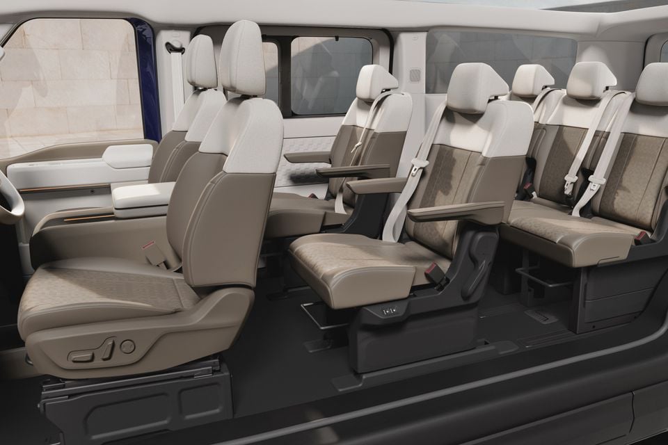 Interior of a Kia PV7 van showing multiple rows of premium beige and tan captain's chairs with fold-out tray tables and seatbelts