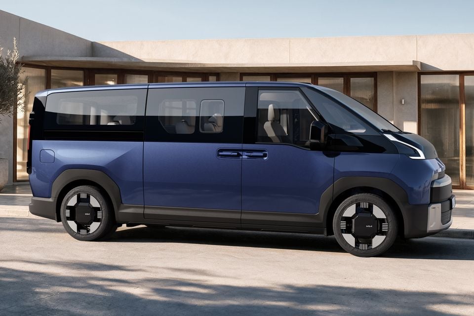 A blue Kia PV7 electric van seen from the side, parked outside a modern building