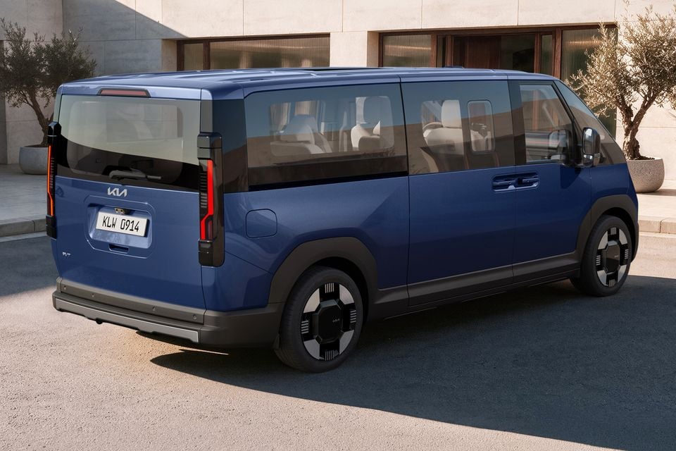 A blue 2027 Kia PV7 van seen from the rear three-quarter angle, parked outside a modern building