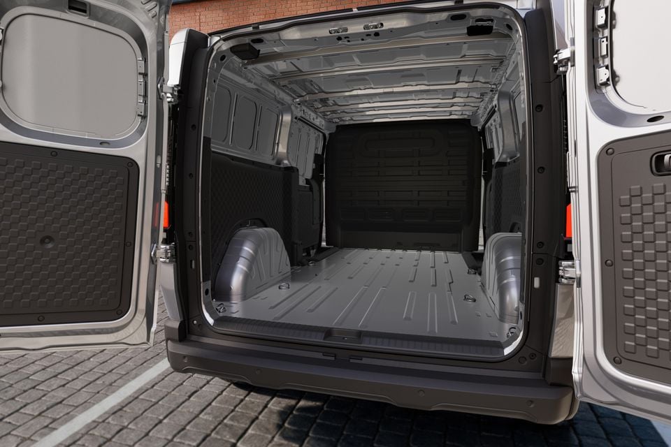 Empty cargo area of a van with rear doors open, showing a large flat load floor and plastic wheel arch covers