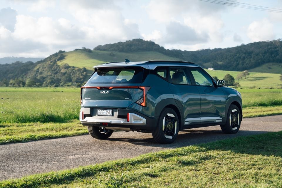 A blue 2027 Kia Seltos Sport hybrid SUV parked on a country road, seen from the rear with green hills behind
