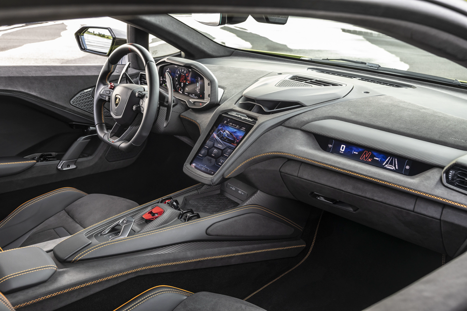 The interior of a Lamborghini Temerario shows its steering wheel, digital gauge cluster and centre console with carbon-fibre trim and orange stitching.