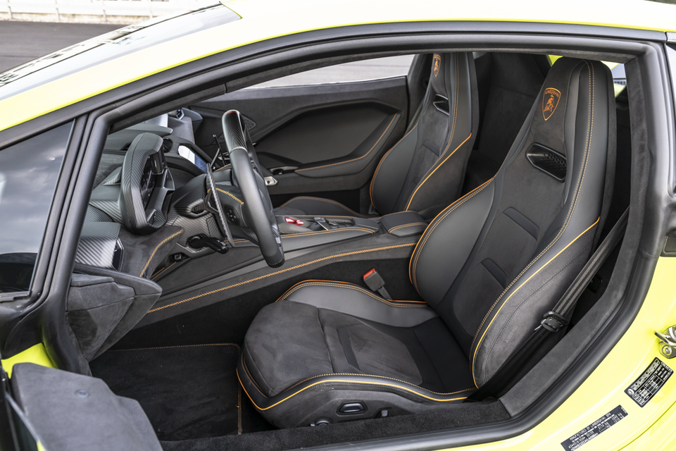 The black and orange leather interior of a 2027 Lamborghini Temerario, showing bucket seats and steering wheel viewed through the open door.