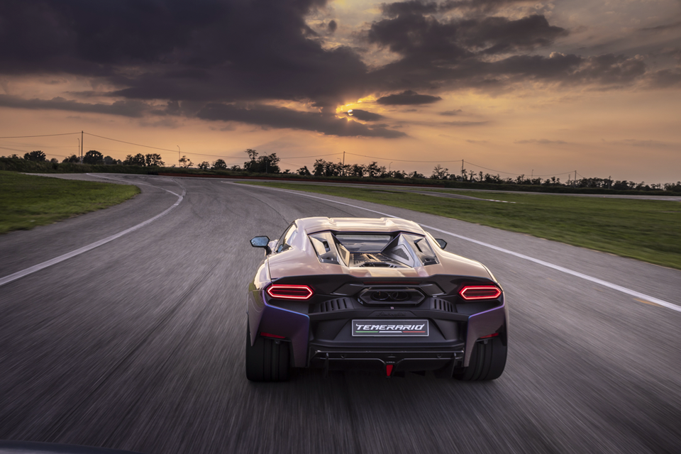 A Lamborghini Temerario sports car speeds away on a race track at sunset, viewed from the rear