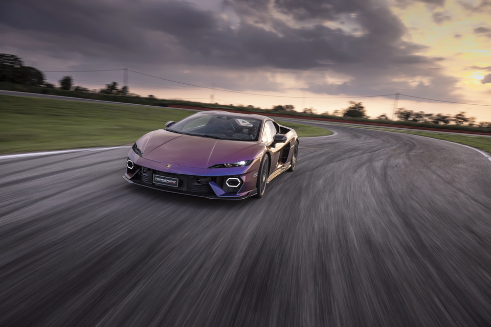 A purple Lamborghini Temerario sports car driving fast around a racetrack corner at dusk.
