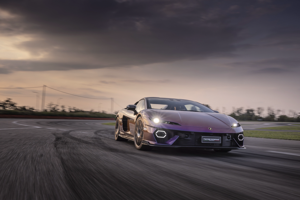 A purple Lamborghini Temerario sports car driving fast on a race track at dusk, seen from the front quarter.