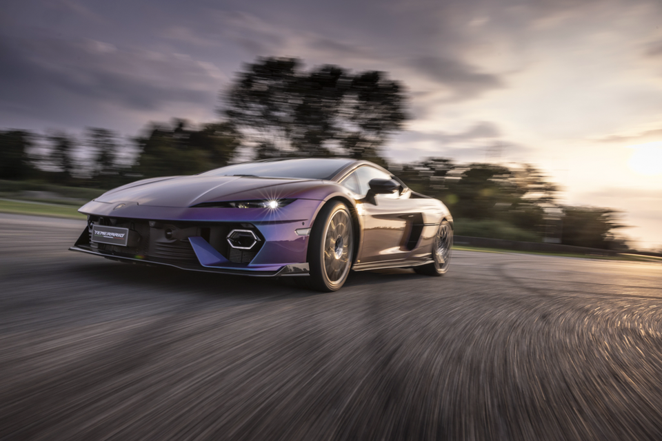 A purple 2027 Lamborghini Temerario sports car driving fast on a track, seen from the front quarter at dusk.