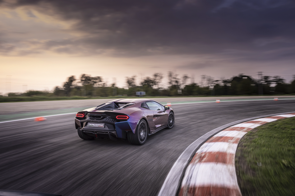 A purple Lamborghini Temerario supercar drives fast around a race track corner, seen from the rear.