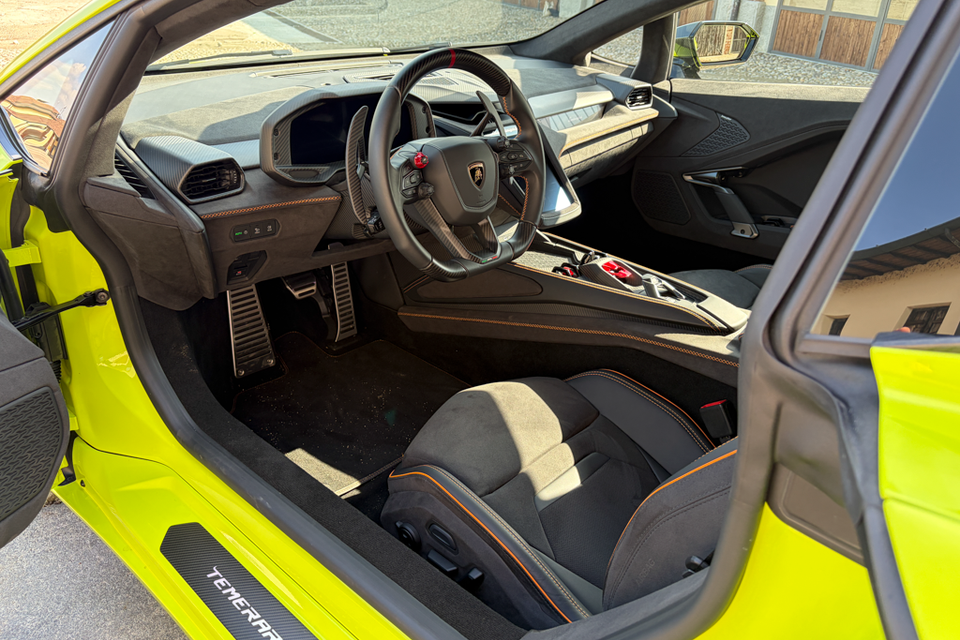 Interior view of a 2027 Lamborghini Temerario with a bright yellow exterior, showing the steering wheel, dashboard and seats through the open door