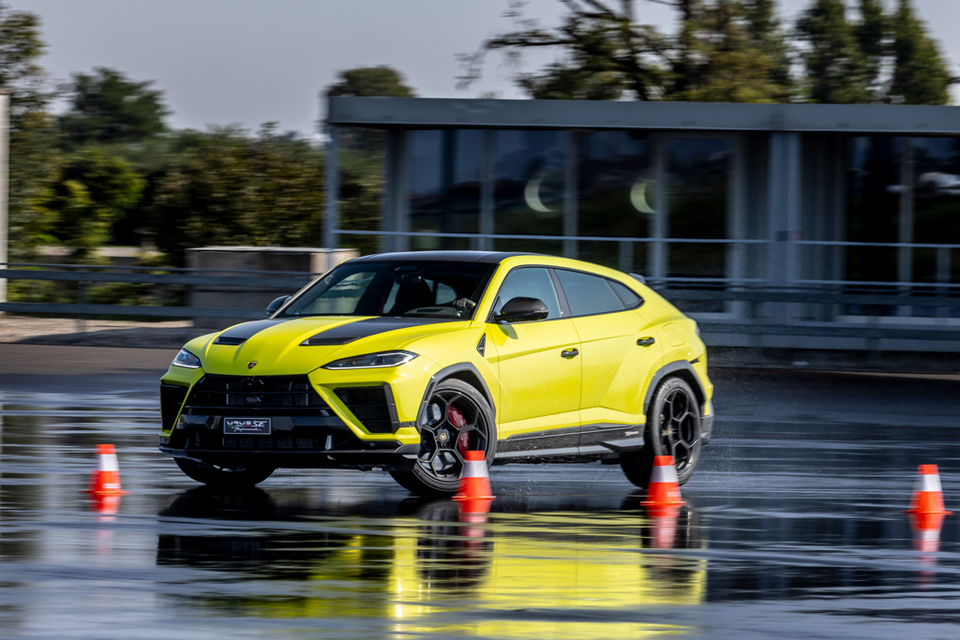 A yellow 2027 Lamborghini Urus SE Performante SUV with black bonnet stripes cornering between cones on a wet test track