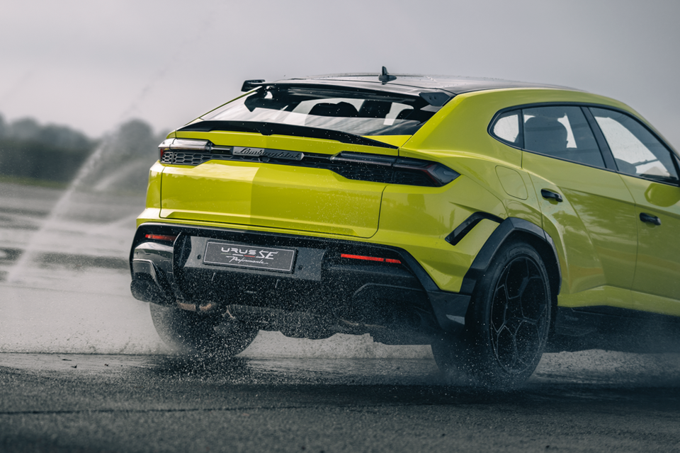 A lime green 2027 Lamborghini Urus SE Performante SUV seen from the rear as it drives across a wet track, kicking up spray