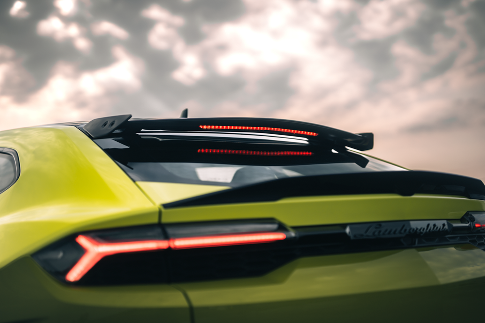 Close-up of the rear spoiler, tail-light and Lamborghini badge on a lime green Lamborghini Urus SE Performante under a cloudy sky