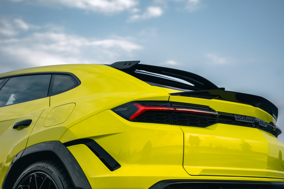 Rear quarter detail of a yellow 2027 Lamborghini Urus SE Performante showing its large rear spoiler, slim tail-light and carbon wheel arch