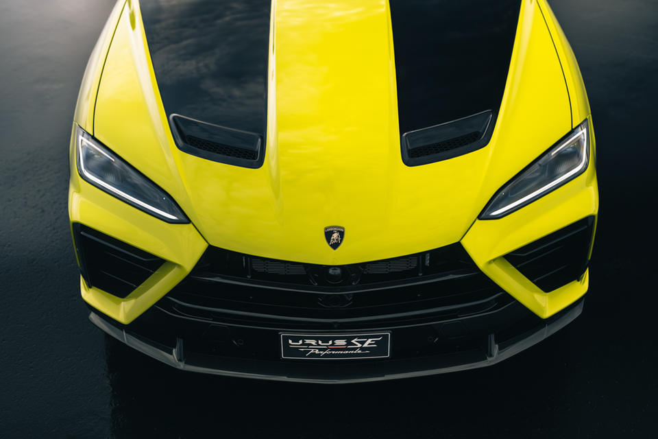 Front end of a yellow 2027 Lamborghini Urus SE Performante seen from above, showing its black bonnet stripes, vents, headlights and grille