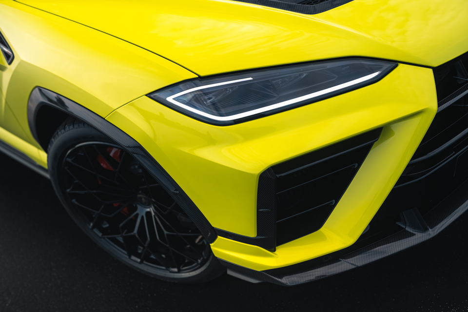 Close-up of the front corner of a yellow 2027 Lamborghini Urus SE Performante, showing its headlight, carbon-fibre air intake and black wheel