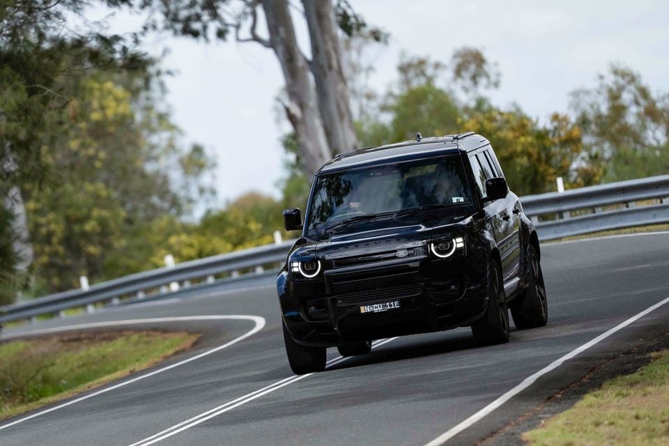 A black Land Rover Defender SUV driving along a winding Australian road, seen from the front