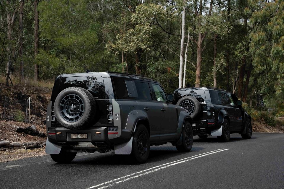 Two dark Land Rover Defenders seen from the rear, parked on a road surrounded by Australian bushland