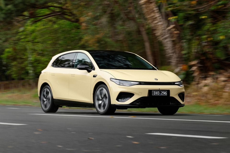 A pale yellow 2027 Leapmotor B05 hatchback driving along a tree-lined road, seen from the front three-quarter angle.