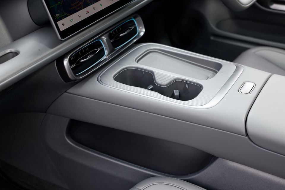 Grey centre console of the 2027 Leapmotor B05 with cupholders, wireless phone tray, blue-lit air vents and lower storage shelf below the touchscreen