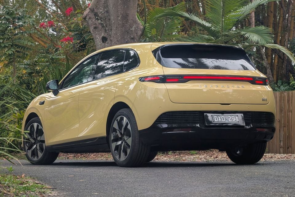 A yellow 2027 Leapmotor B05 electric hatchback parked on a driveway, seen from the rear and side with tropical plants behind