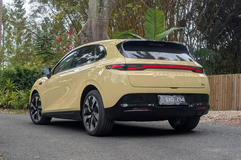 A pale yellow 2027 Leapmotor B05 hatchback parked on a driveway, seen from the rear driver's side with a full-width tail-light bar