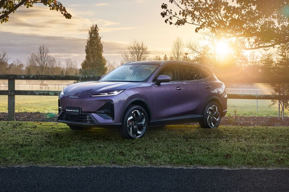 A purple Lepas L6 EV SUV seen from the front-side angle, parked on grass beside a wooden fence at sunset.