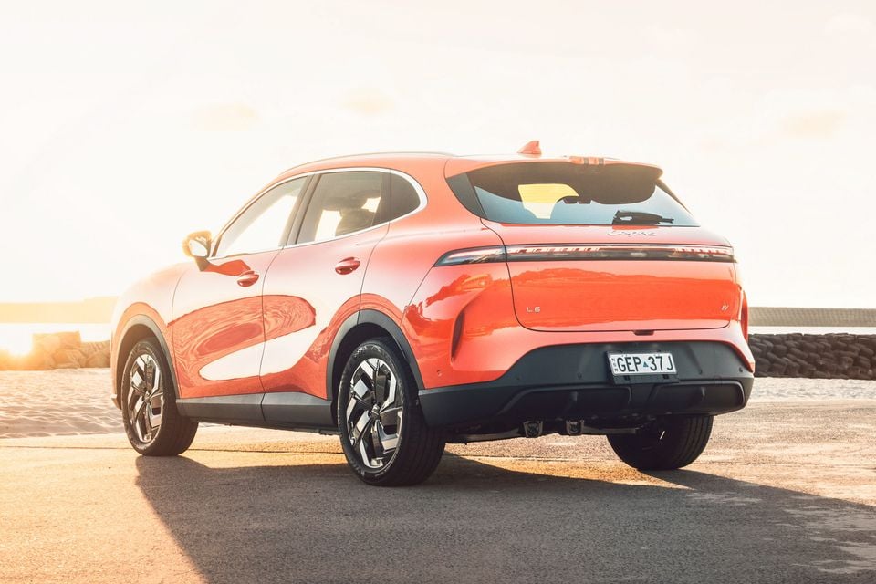 An orange 2027 Lepas L6 Signature EV SUV parked on a seaside road at sunset, seen from the rear passenger side