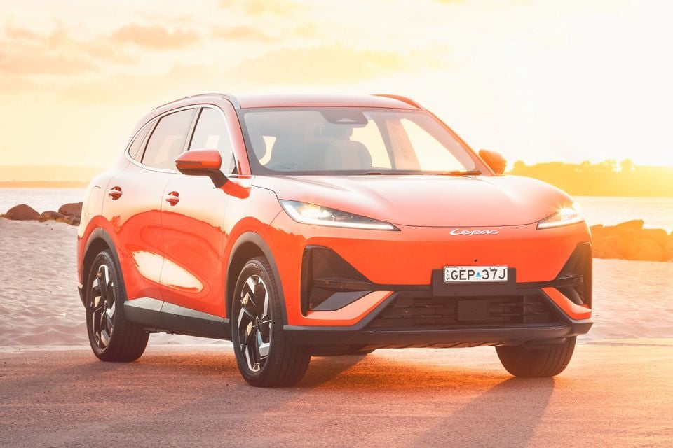 An orange 2027 Lepas L6 Signature electric SUV parked by a sandy beach at sunset, seen from the front right