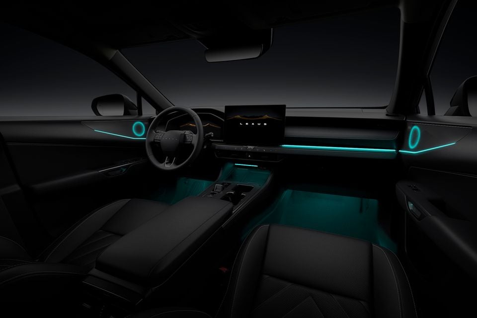 Lexus NX interior at night showing teal ambient lighting across the dashboard, centre console, and footwell, with a large central infotainment screen displaying the Lexus logo