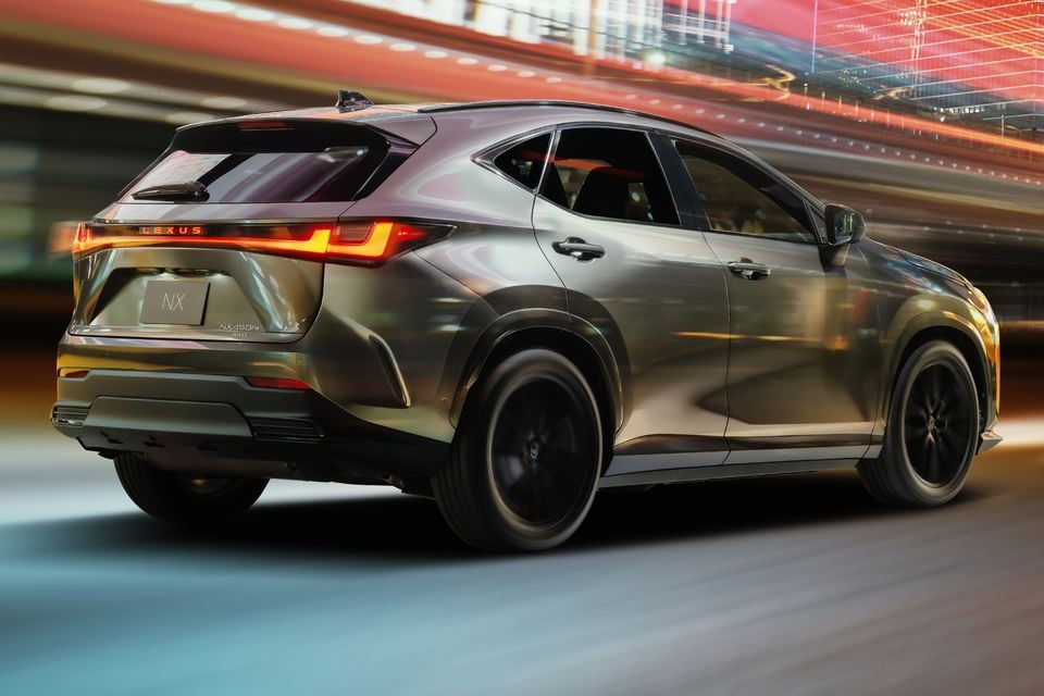 Lexus NX 450h+ AWD SUV seen from the rear three-quarter angle, moving through a city environment at night