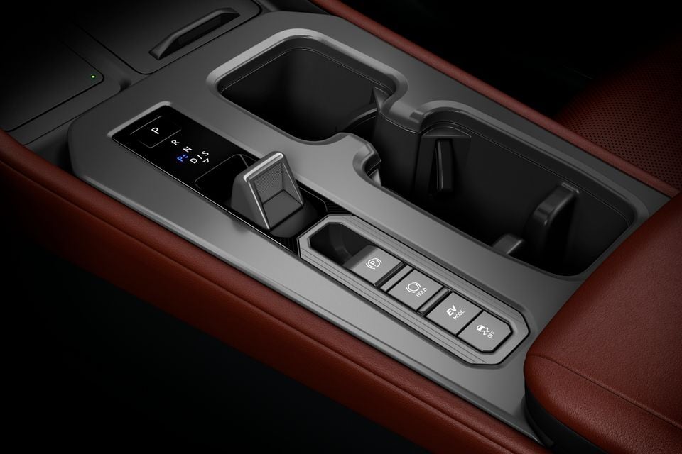 Close-up of the centre console in a Lexus NX facelift, showing a sliding gear selector, EV mode and hold buttons, and a cup holder with red leather trim