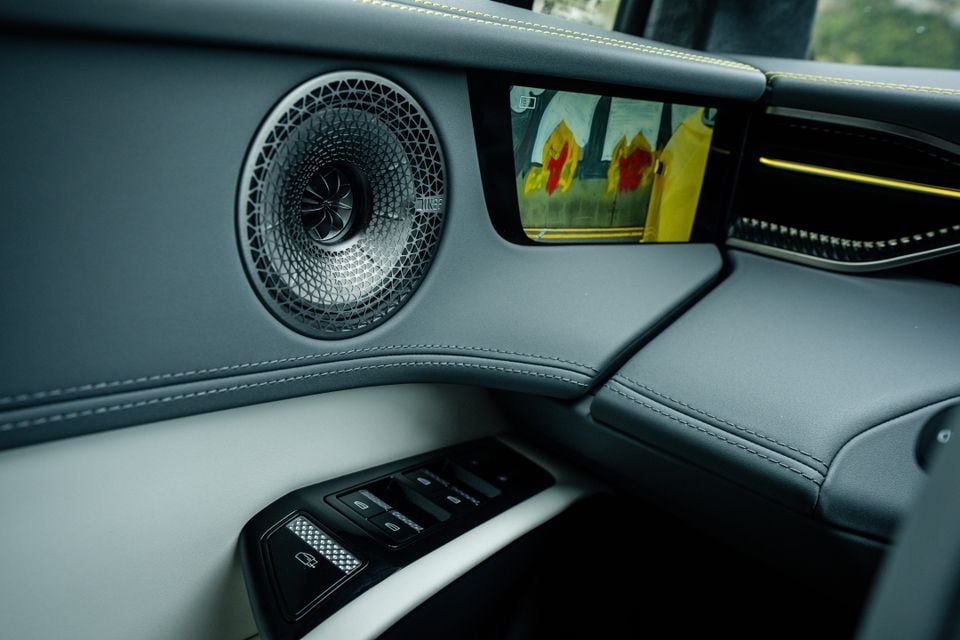 Door panel of the 2027 Lotus Eletre X with a KEF speaker, digital side mirror camera screen, window switches and grey leather trim with yellow stitching