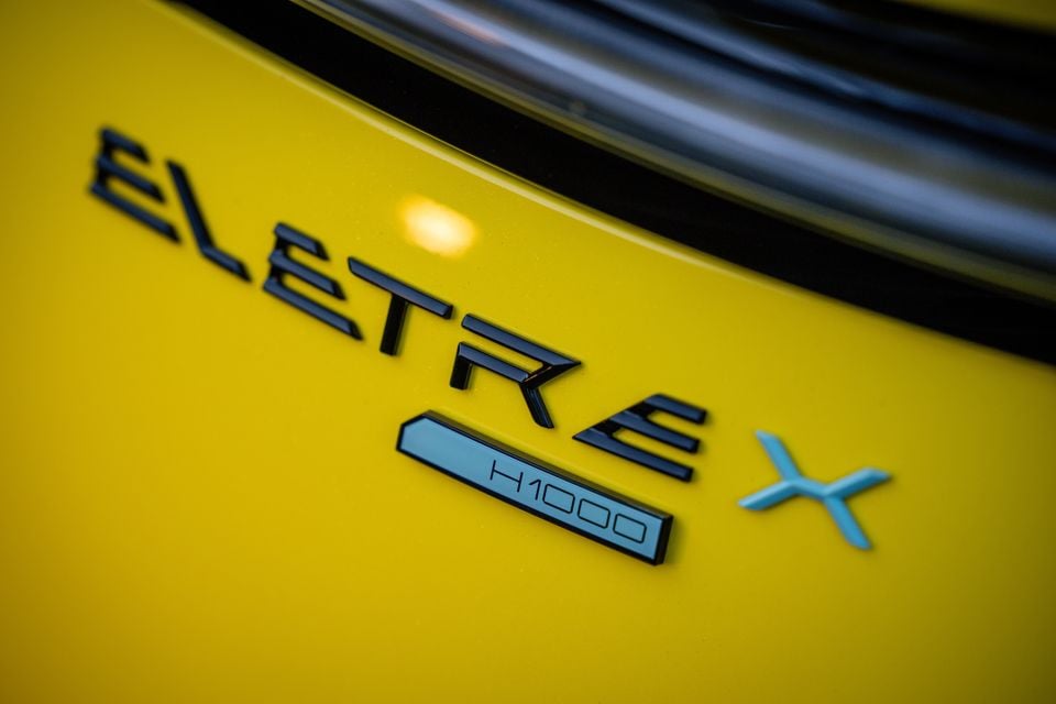 Close-up of the black Eletre X badge with an H1000 plaque on the yellow bodywork of a 2027 Lotus Eletre X