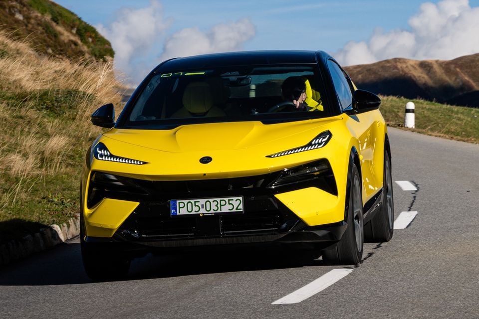 A yellow 2027 Lotus Eletre X SUV driving along a winding mountain road, seen from the front