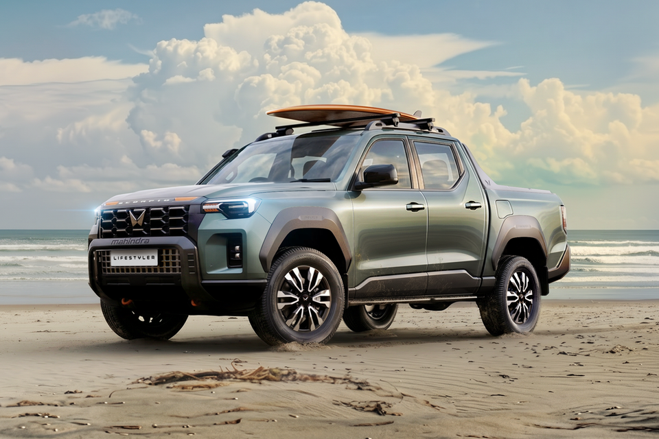 A green Mahindra Scorpio Lifestyler dual-cab ute parked on a beach with a surfboard on the roof rack, seen from the front-side