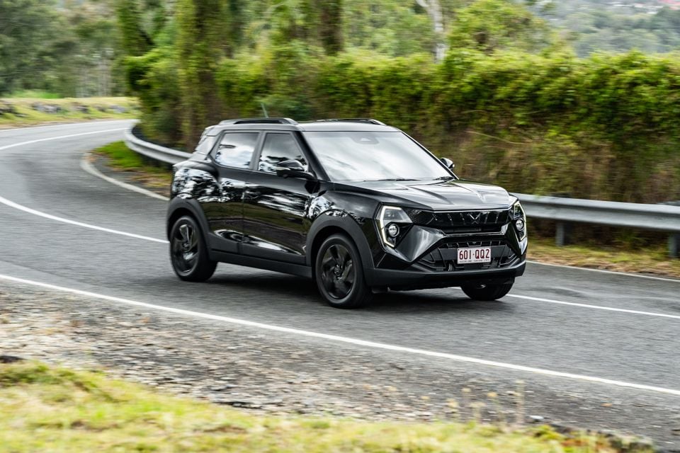 A black Mahindra XUV 3XO SUV driving along a winding road surrounded by green trees