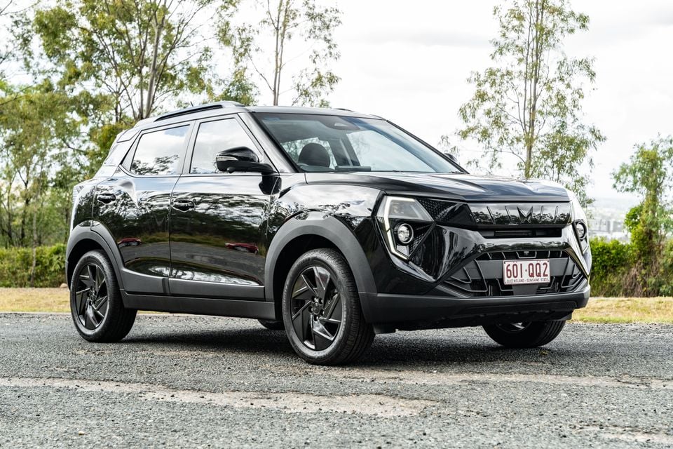 A black Mahindra XUV 3XO SUV seen from the front-left side, parked on a gravel surface with trees in the background, wearing Queensland registration plates.
