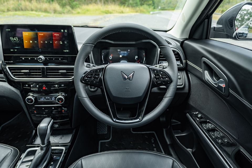 Interior view of a Mahindra XUV 3XO showing the steering wheel with Mahindra logo, touchscreen infotainment system, digital instrument cluster, and centre console