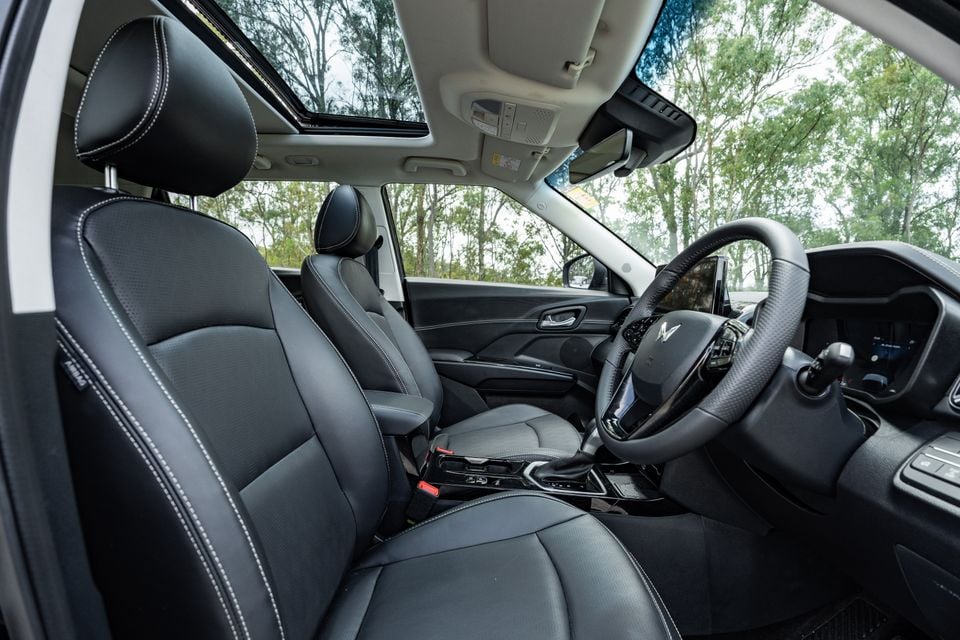 Interior view of a Mahindra XUV 3XO showing the front seats, steering wheel, centre console and sunroof, with dark leather upholstery and white contrast stitching