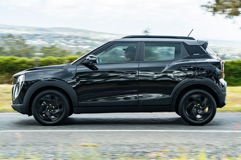 A black Mahindra XUV 3XO Black Edition small SUV seen from the side while driving on a road with a green hillside background