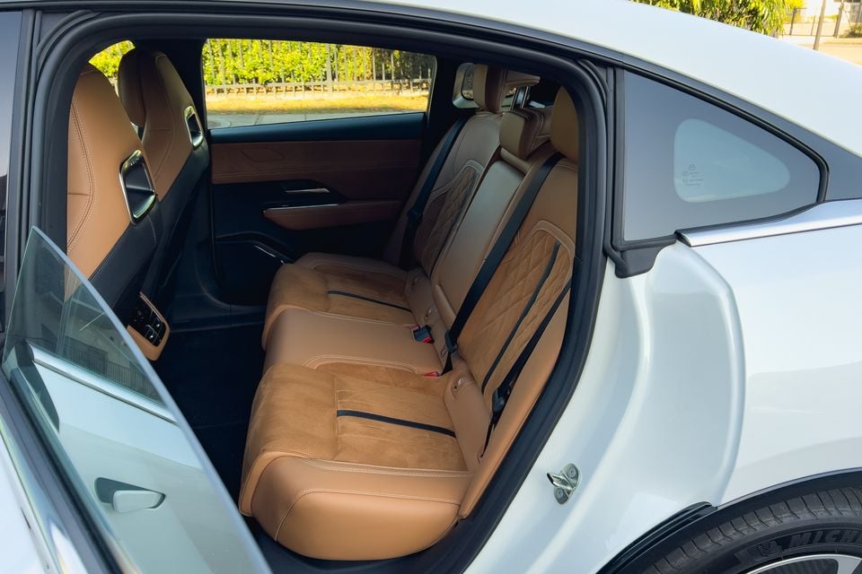 The tan leather rear seats of a 2027 Mazda 6e Atenza, viewed through the open door of the white sedan.