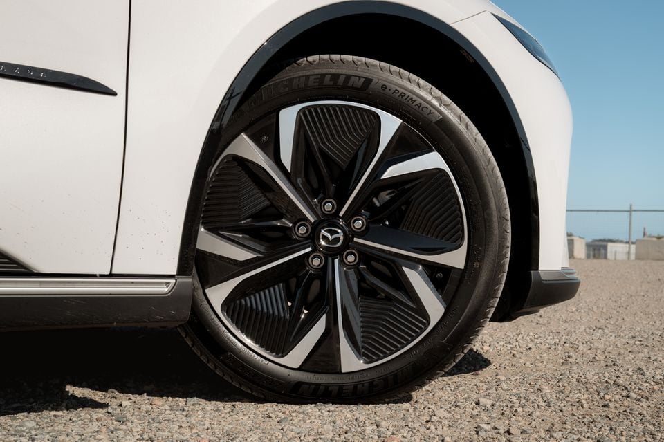 Close-up of the front wheel and alloy rim on a white 2027 Mazda 6e Atenza sedan.
